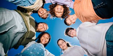 Group of diverse friends smiling in a circle looking down at the camera.