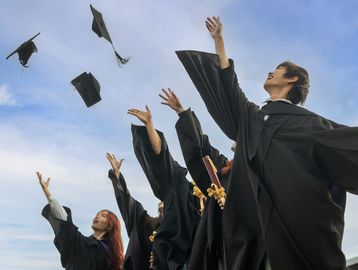 Graduates in black gowns throwing caps into the air celebrating.