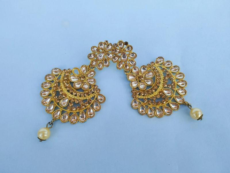Ornate gold crescent earrings decorated with many small clear sparkling stones.