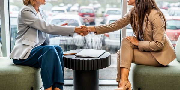 Two businesswomen shaking hands across a table in a modern office setting.