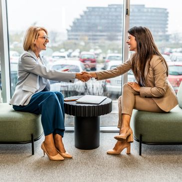 Two professional women shaking hands in an office setting.