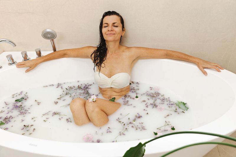 A serene woman enjoys a milky bath with lavender petals, relaxing in a modern bathroom. The peaceful scene conveys wellness, selfcare, and inner calm during a tranquil spa-inspired moment.