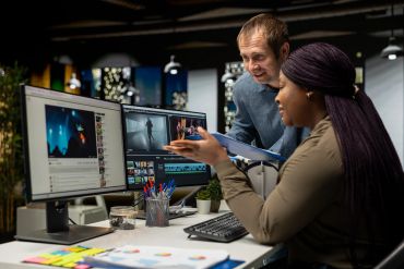 Two coworkers discussing video editing at a workstation.