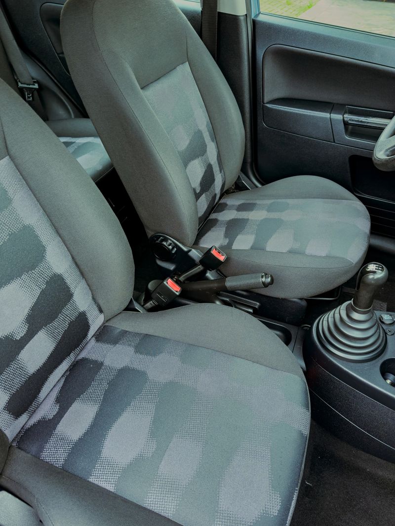 The inside of a modern vehicle highlights two comfortable front seats with sleek upholstery and a detailed gear shifter, all set in a well-lit parking spot under a clear sky.