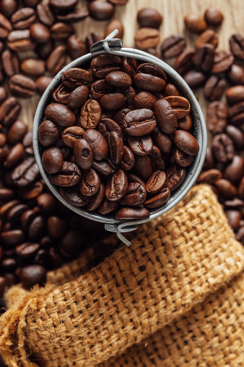A rustic scene featuring freshly roasted coffee beans in a metal bucket atop a wooden surface, surrounded by burlap. Ideal for coffee enthusiasts and culinary themes.