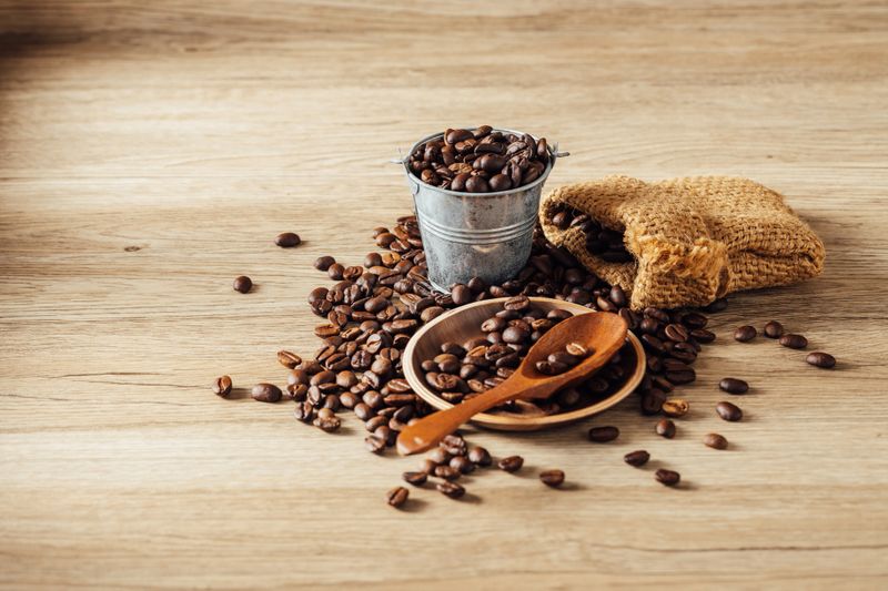 A captivating arrangement of coffee beans spilled across a rustic wooden table, accompanied by a wooden spoon and metal pot, showcasing natural textures and warmth.