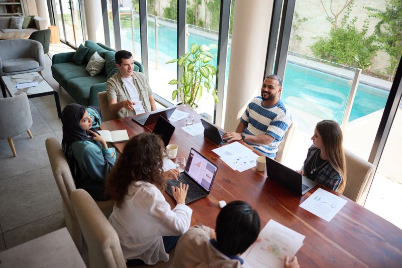 High angle view of business professionals discussing ideas in team meeting. Entrepreneurs are sitting with laptops around table. They are sharing ideas.