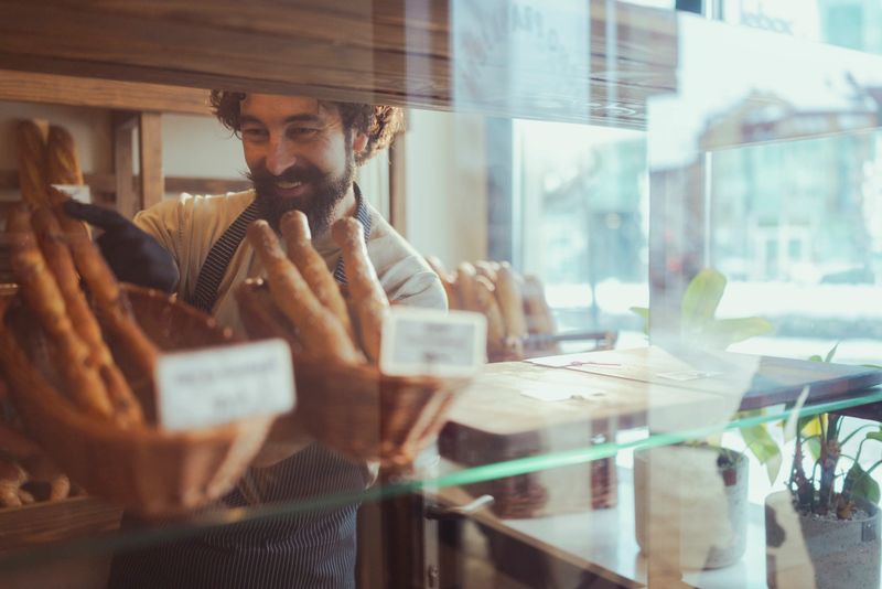 Smiling Bearded Baker Arranging Fresh Bread in Artisan Bakery