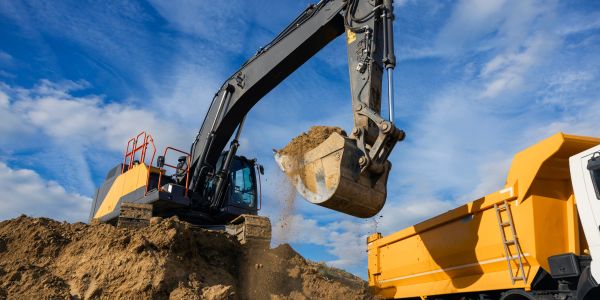 Excavator loading soil into dump truck at a construction site.