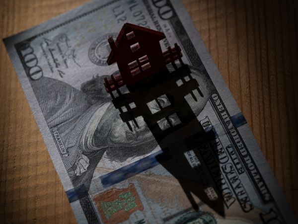 A small house model casting a shadow on a $100 bill.
