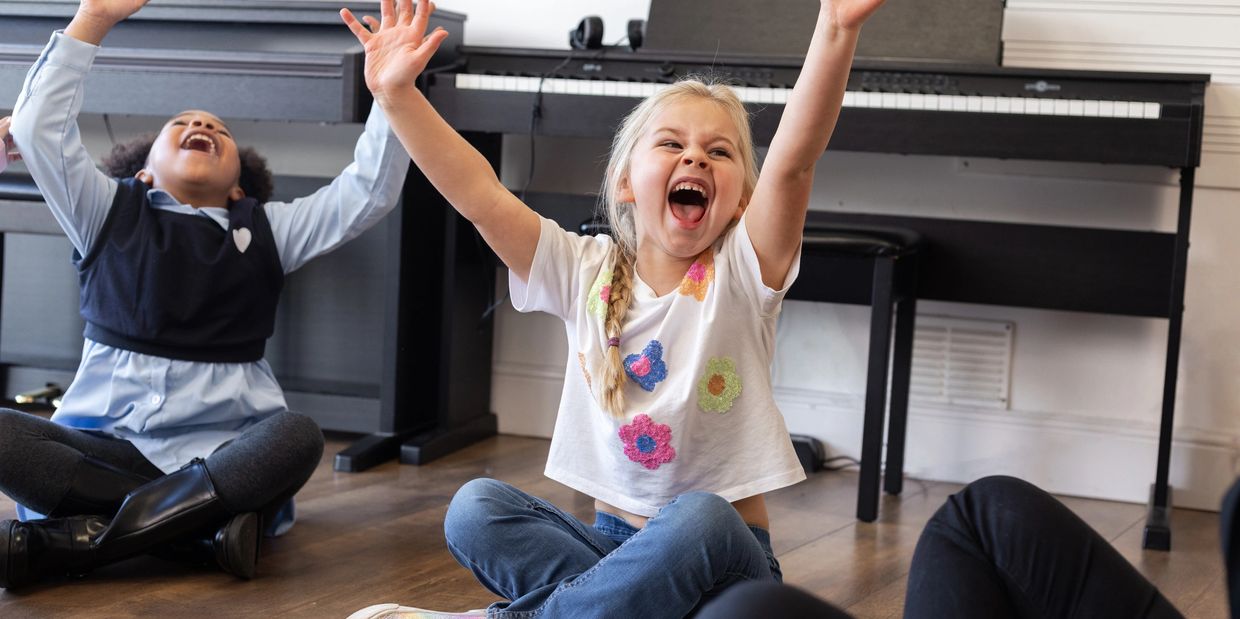Three children sitting on the floor with arms raised, laughing joyfully.