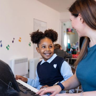 A young girl smiling while playing piano with an adult.
