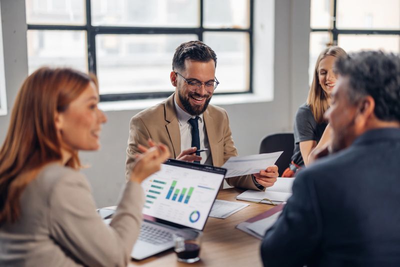 A lively meeting where team members engage in discussions while analyzing data reports on their laptop, fostering collaboration and creativity in a modern office space.