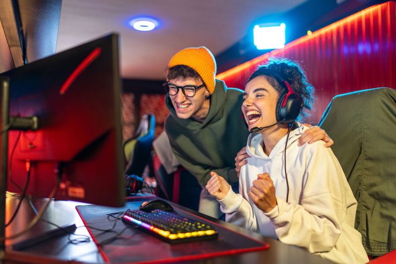 Young woman with headphones and male friend celebrate a gaming victory in a vibrant esports arena, smiling, cheering, and sharing excited teamwork and joy before monitors