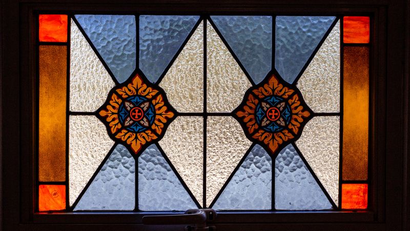 Stained glass window featuring decorative floral and cross patterns in orange, blue, and clear textured glass