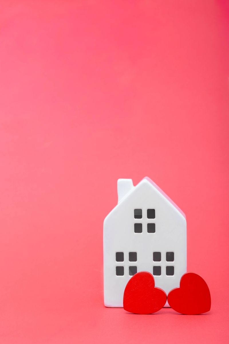 Ceramic house model with red heart shapes in front, placed on a vibrant pink background, representing love, home, and warmth in a cozy setting