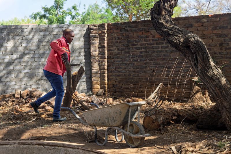 african construction worker with a wheelbarrow cleaning rubble and wood in a yard