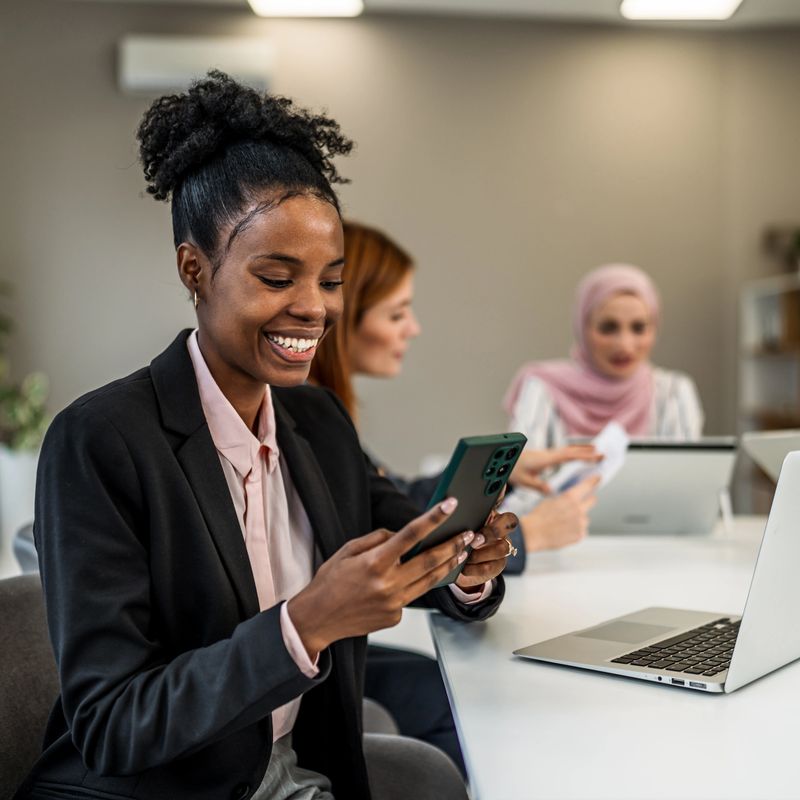 Smiling african american businesswoman using a smartphone during an office meeting with diverse colleagues