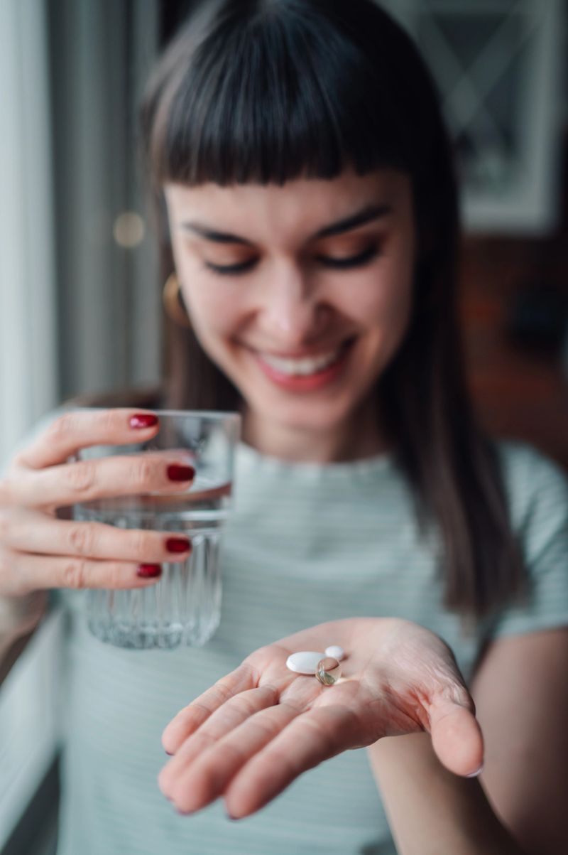 Smiling young woman holding vitamin pills in hand and a glass of water, focusing on daily health and wellness