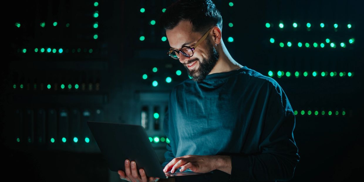 Man working on a laptop with a smile in a dimly lit room with green lights.
