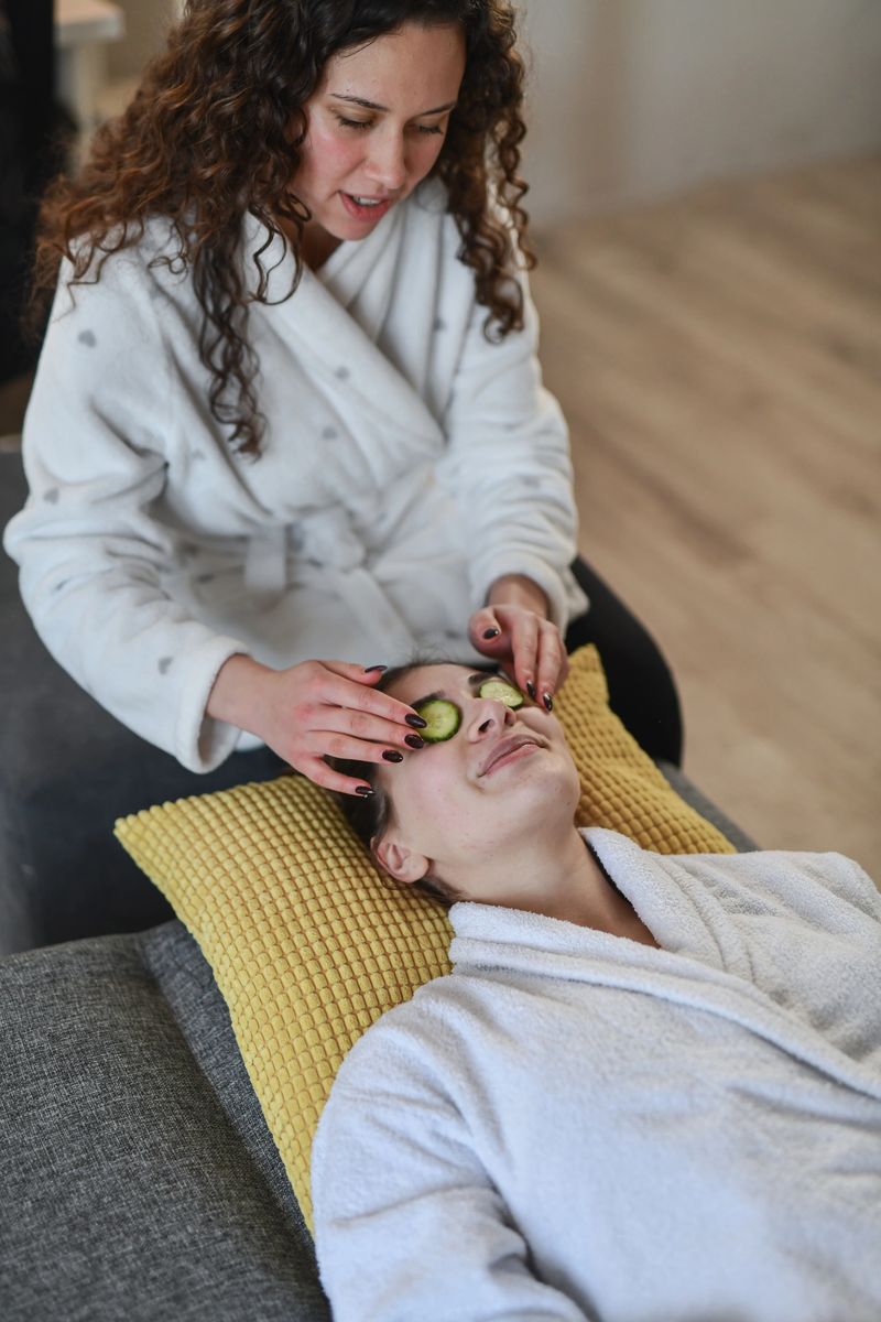 Two women enjoy a tranquil spa day as one performs a jade roller facial massage on the other. Robes, cushions, and a spa setting create a calm, pampering moment.