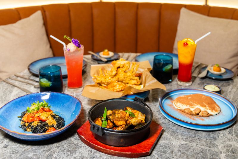 Gourmet meal setup in modern restaurant, featuring seafood pasta, fried dish, desserts, and cocktails. Elegant dining setting for foodies, gastronomy enthusiasts. Vibrant color, luxury ambiance.