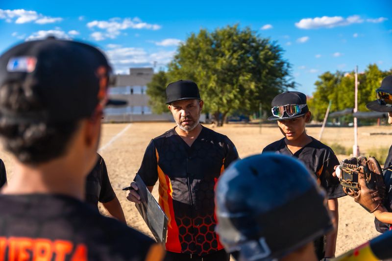 Dedicated coach giving hands-on instruction and strategy to a youth baseball team during sunny outdoor practice, fostering teamwork, skill development, and focus on the field