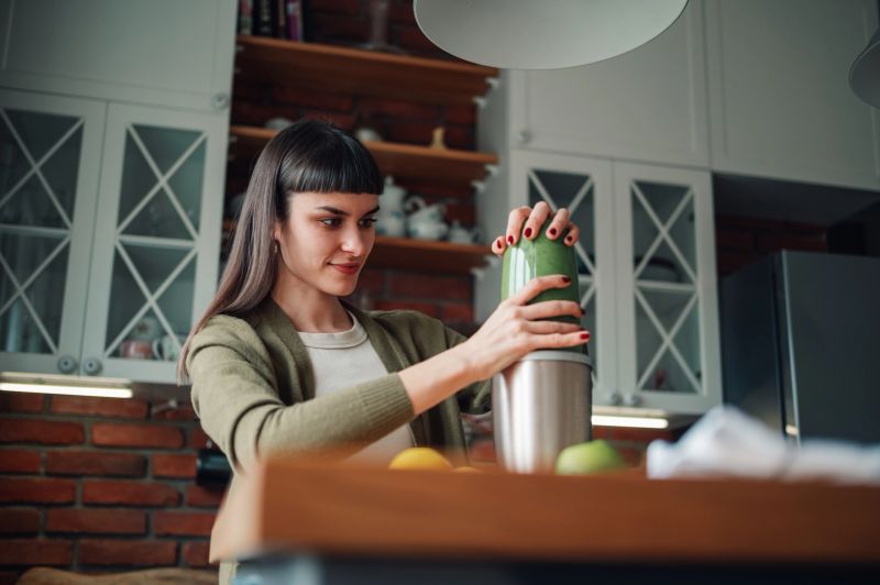 Young woman preparing a fresh, green health smoothie in her kitchen, focusing on wellness and nutritious breakfast