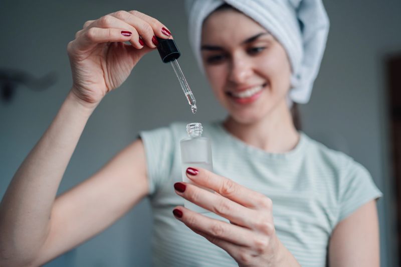 Young adult woman smiling, performing her morning skincare routine, applying a facial serum with a pipette