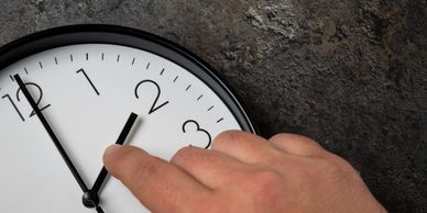 A hand adjusting the time on a white wall clock.