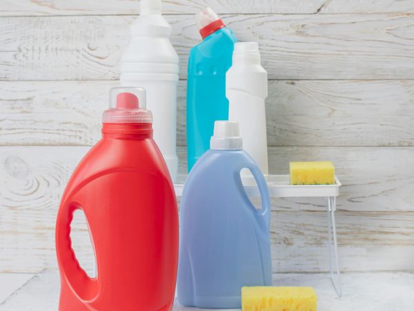 Various colorful cleaning bottles and sponges on a white surface.