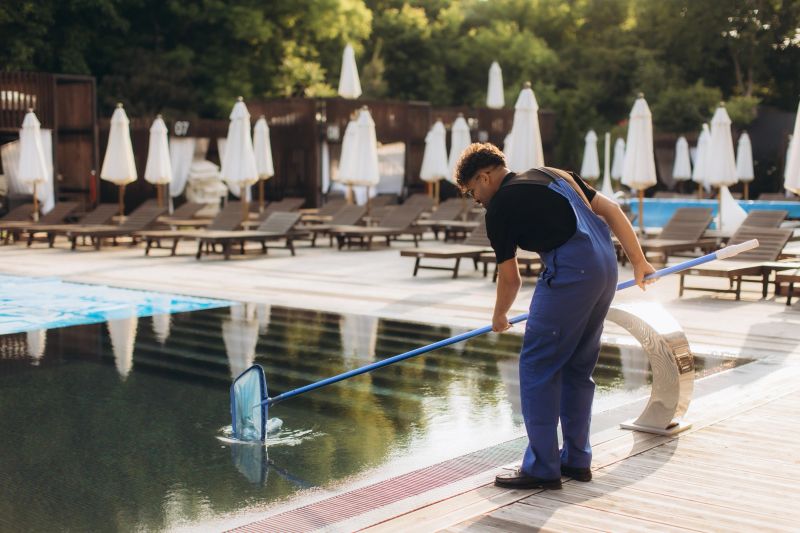 Pool cleaner diligently maintaining a sparkling swimming pool during summer, using a cleaning net to remove leaves and debris