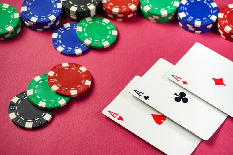The poker game takes place on a bright pink table with three aces surrounded by colorful chips. The players seem engaged, and the atmosphere is lively.