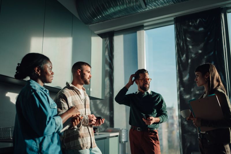 Group of diverse colleagues talking and sharing ideas at a modern office during a coffee break, fostering teamwork and collaboration