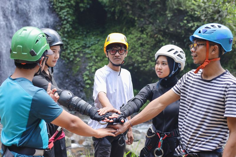 Group of Asian Diverse Group Place Their Hands in the Center of a Circle, Prepares for an Extreme Waterfall Rappelling Excursion