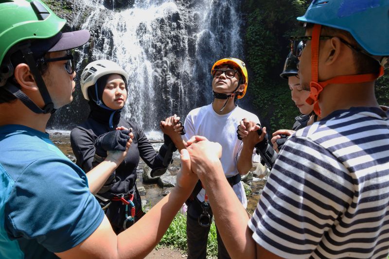 Group Of Diverse Friends Standing In Circle And Holding Hands In Prayer Before Starting Canyoning Adventure In Front Of Waterfall