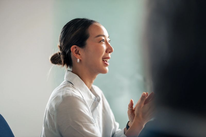 Asian businesswoman speaking confidently in a corporate meeting, engaging colleagues with ideas and gestures, projecting leadership, professionalism and collaborative energy in a modern office