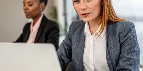 Two professional women working intently on laptops in an office setting.