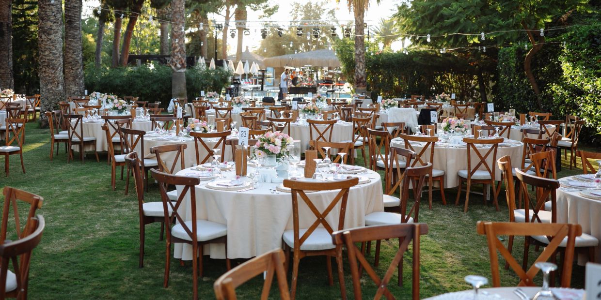 Outdoor wedding reception setup with decorated round tables and wooden chairs.