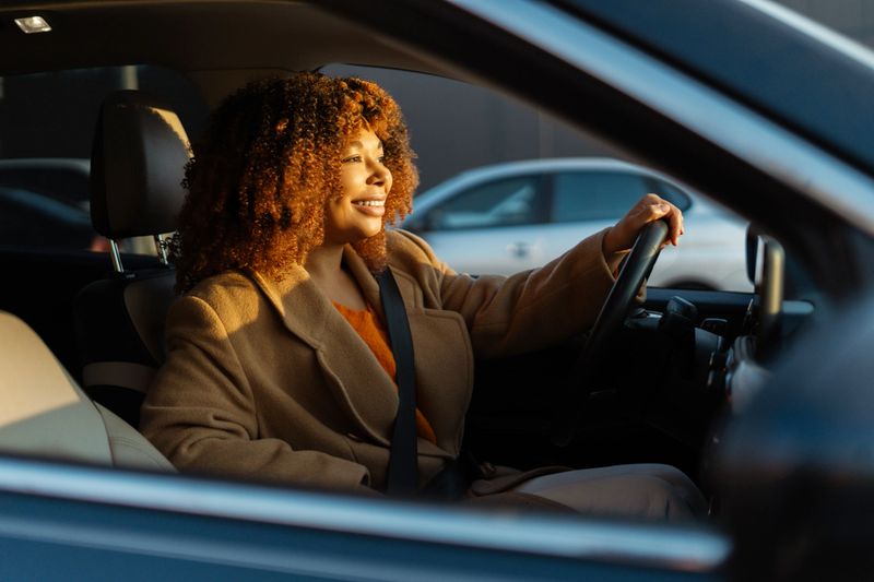 Woman smiling while driving car during golden hour, enjoying freedom and commute