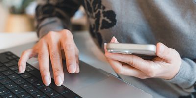 Person multitasking with a smartphone and laptop keyboard.