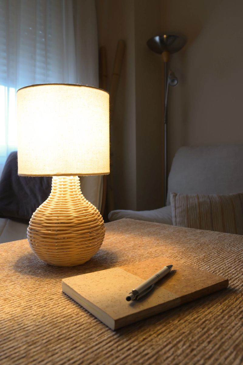 Desk lamp casts warm glow over notebook and pen on a textured wooden table, evoking cozy, eco-conscious home office life focused on planning, study and sustainable living