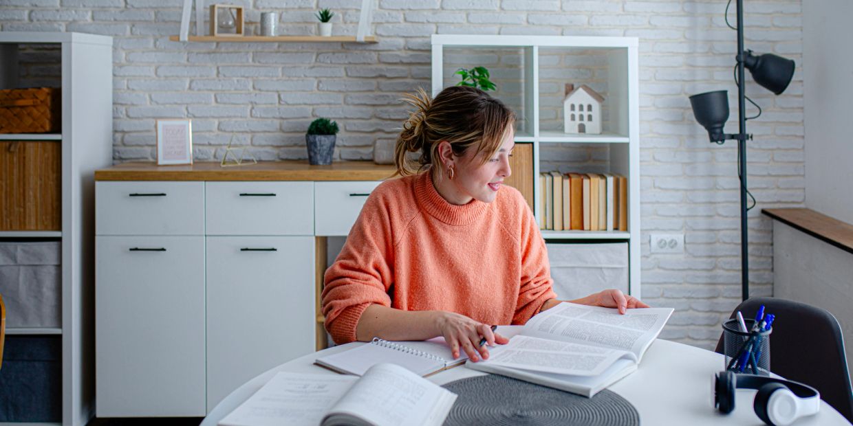 Woman reading and studying with multiple books at a white table.