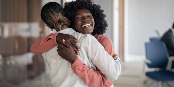 Two women sharing a joyful hug indoors.
