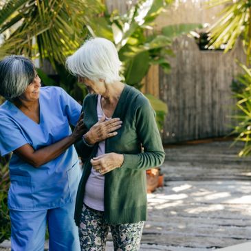 Caregiver comforting elderly woman outdoors in a garden setting.