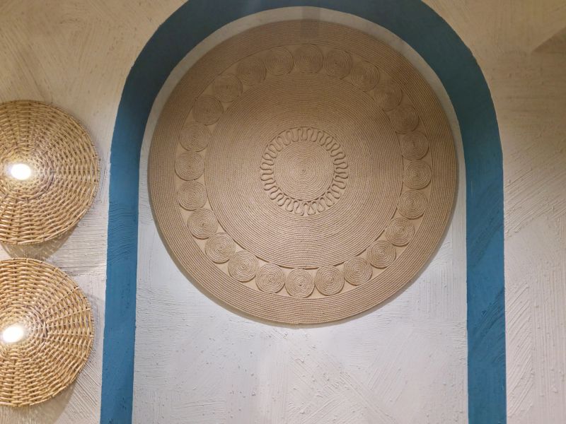 Round jute rope wall art on a textured white wall with a blue arch. Natural woven decor for interior design and home decoration.