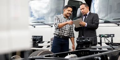 Two men discussing truck parts and using a tablet.