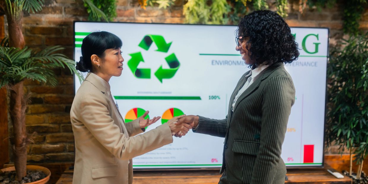 Deux femmes se serrent la main devant un écran de recyclage.