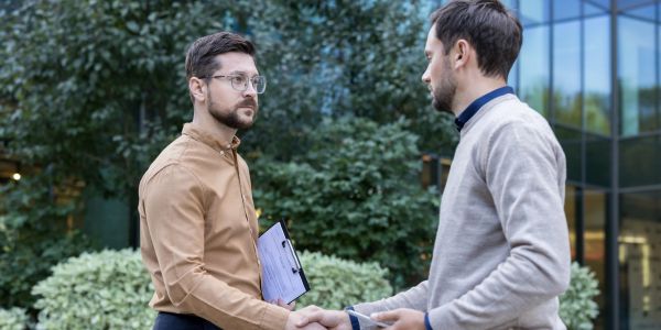Two men shaking hands outdoors near a building.