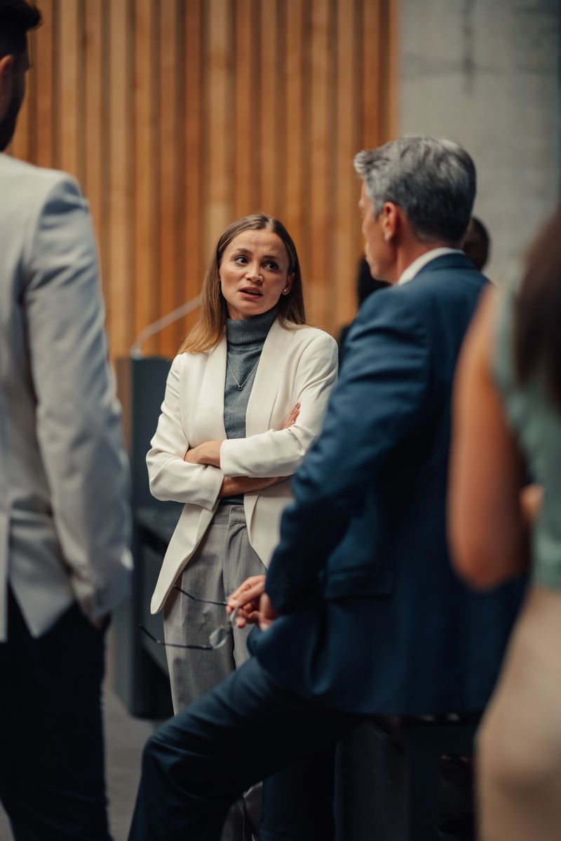 Businesswoman standing with crossed arms, thoughtfully engaging in a conversation with colleagues during a corporate networking event
